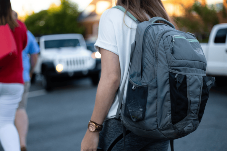 a photo of a girl wearing a North Face backpack with a white Jeep in the background.